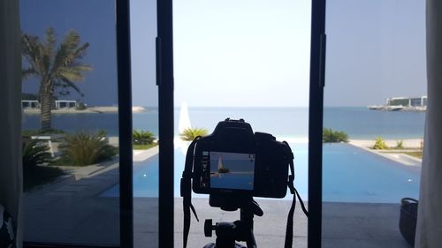 Close-up of camera by window photographing sea