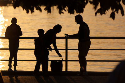 Silhouette people standing by sea against sky during sunset