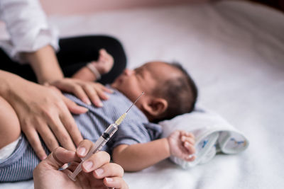 Cropped hand holding syringe with family in background