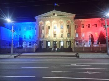 Illuminated street by buildings in city at night
