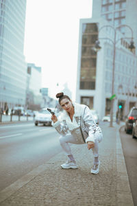 Portrait of woman crouching on footpath in city