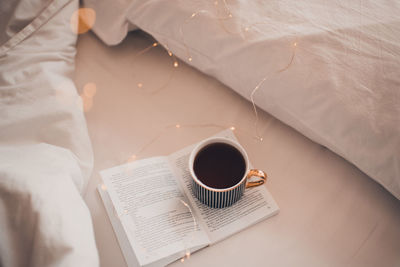 Cup of black coffee stay on open paper book in bed on white blanket close up. cozy morning.