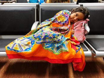 Portrait of cute girl with colorful blanket lying on seat