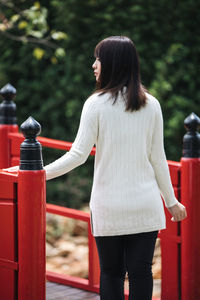 Rear view of woman standing by railing against trees