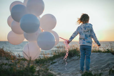 Rear view of girl with balloons at beach