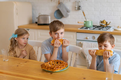 Cheerful children are sitting at table in kitchen, playing with loaf bread