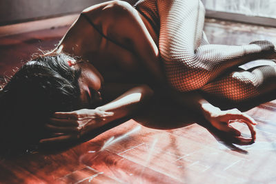 High angle view of woman wearing fishnet stockings lying on hardwood floor at home