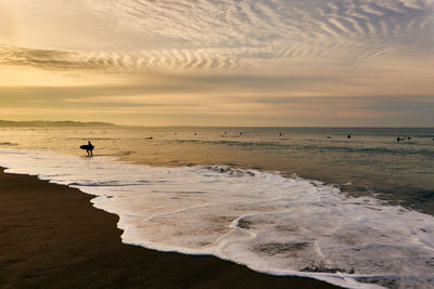 Scenic view of sea with surfers against sky during sunrise