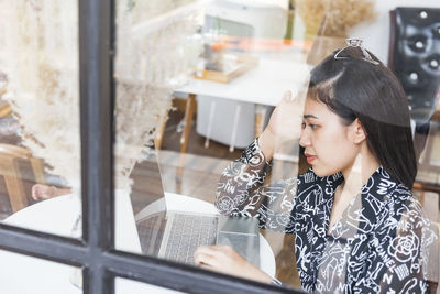 Businesswoman using laptop at cafe seen through window