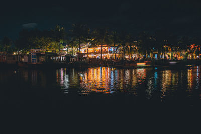 Illuminated buildings by river against sky at night