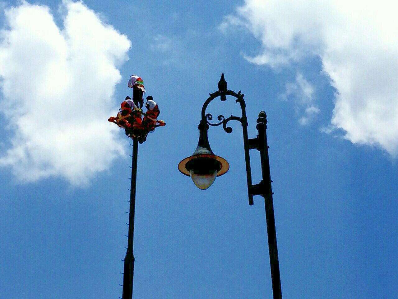 low angle view, sky, lighting equipment, street light, cloud - sky, hanging, cloud, pole, blue, no people, religion, day, cloudy, lantern, spirituality, outdoors, high section, lamp post, human representation, communication