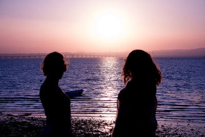 Rear view of silhouette women standing at beach during sunset
