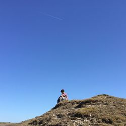 Low angle view of boy sitting on hill against clear sky