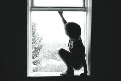 Side view of woman looking through window at home