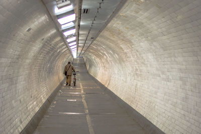 Rear view of man with bicycle walking at greenwich foot tunnel