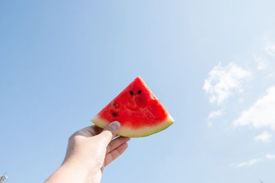 Cropped hand holding watermelon slice against blue sky