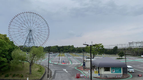 Ferris wheel by road against sky in city