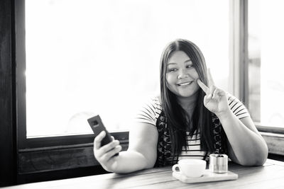 Portrait of smiling young woman using phone on table