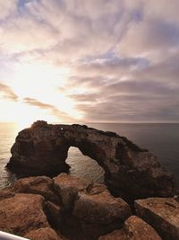 Rock formation on beach against sky during sunset