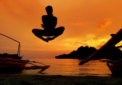 Man jumping at beach against orange sky