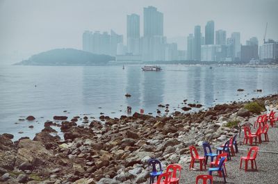 Chairs by sea against city