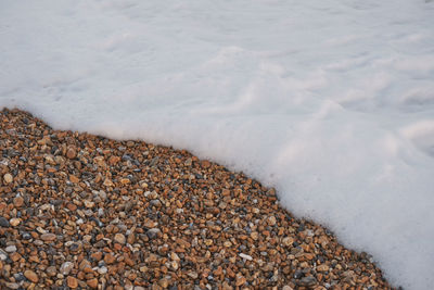 Sea foam washing up onto a pebbled beach