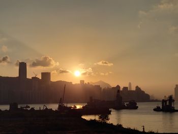 Silhouette buildings by sea against sky during sunset