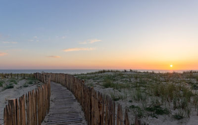 Walkway at beach against sky during sunset