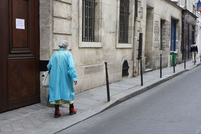 Rear view of man walking on sidewalk by building