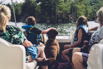 REAR VIEW OF PEOPLE SITTING ON BOAT AGAINST LAKE