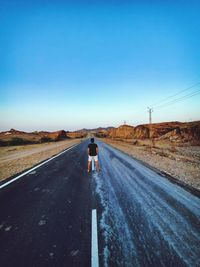 Rear view of man walking on road against clear blue sky