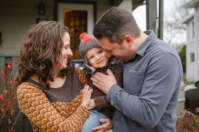 A joyful child is being tenderly held between his mom and dad in yard