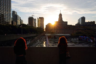 Rear view of woman and buildings against sky during sunset