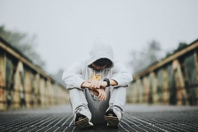 Full length of man sitting on footbridge against sky