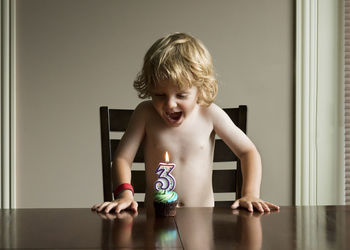 Cheerful boy with mouth open looking at birthday cupcake while standing by table