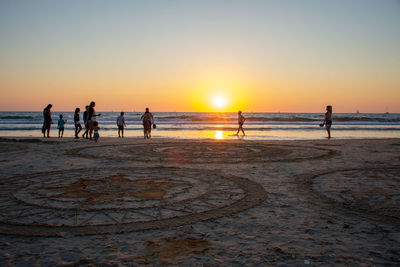 Silhouette people on beach against sky during sunset