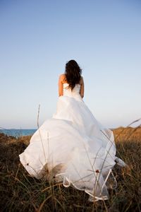 Rear view of bride on field against clear sky