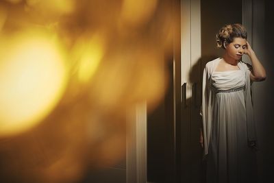 Bride wearing wedding dress while standing against cupboard