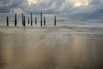 Wooden posts in sea against sky