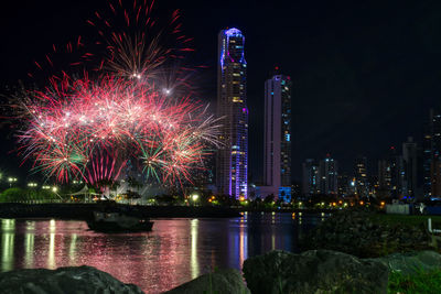 Firework display over river by illuminated buildings in city at night, panama skyline