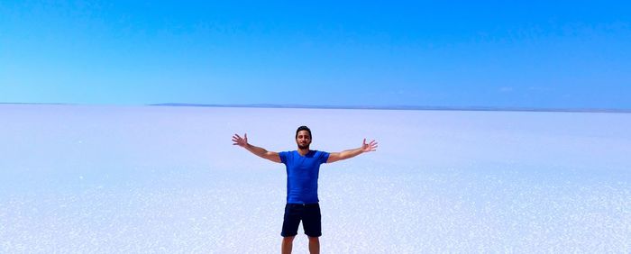 Young man standing on salt flat against clear blue sky