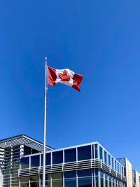 Low angle view of flag against building against blue sky