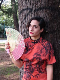 Portrait of woman standing by tree trunk
