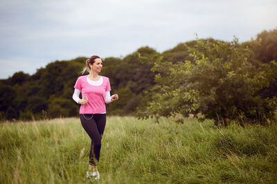 Beautiful woman listening music on headphones while running on grassy field