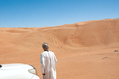 Man on sand dune in desert against clear sky