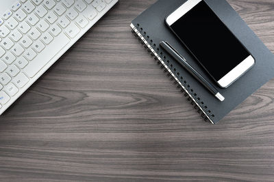 Directly above view of office desk table with computer keyboard, pen, notepad and smartphone.