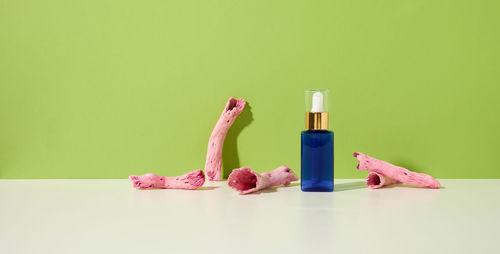 Blue glass bottle with a dropper for cosmetics on a white table, green background. packaging fo