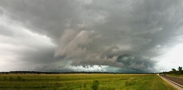 Road passing through field against cloudy sky