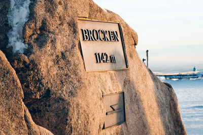 Information sign on rock by sea against sky