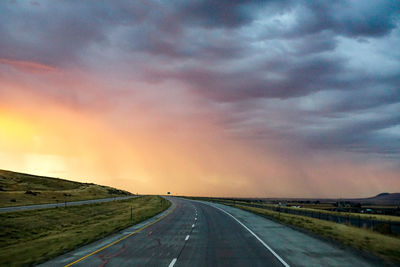 Empty country road along landscape against cloudy sky